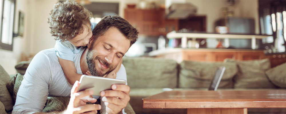 Man on mobile device with child hanging on over back